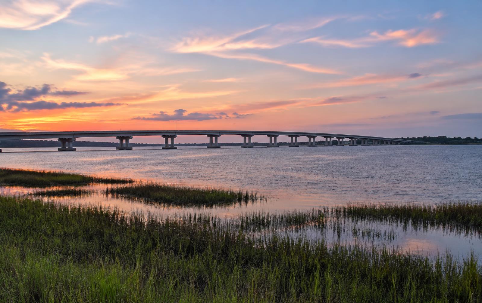 A long bridge crossing the wide St. Johns River at dusk above salt marsh